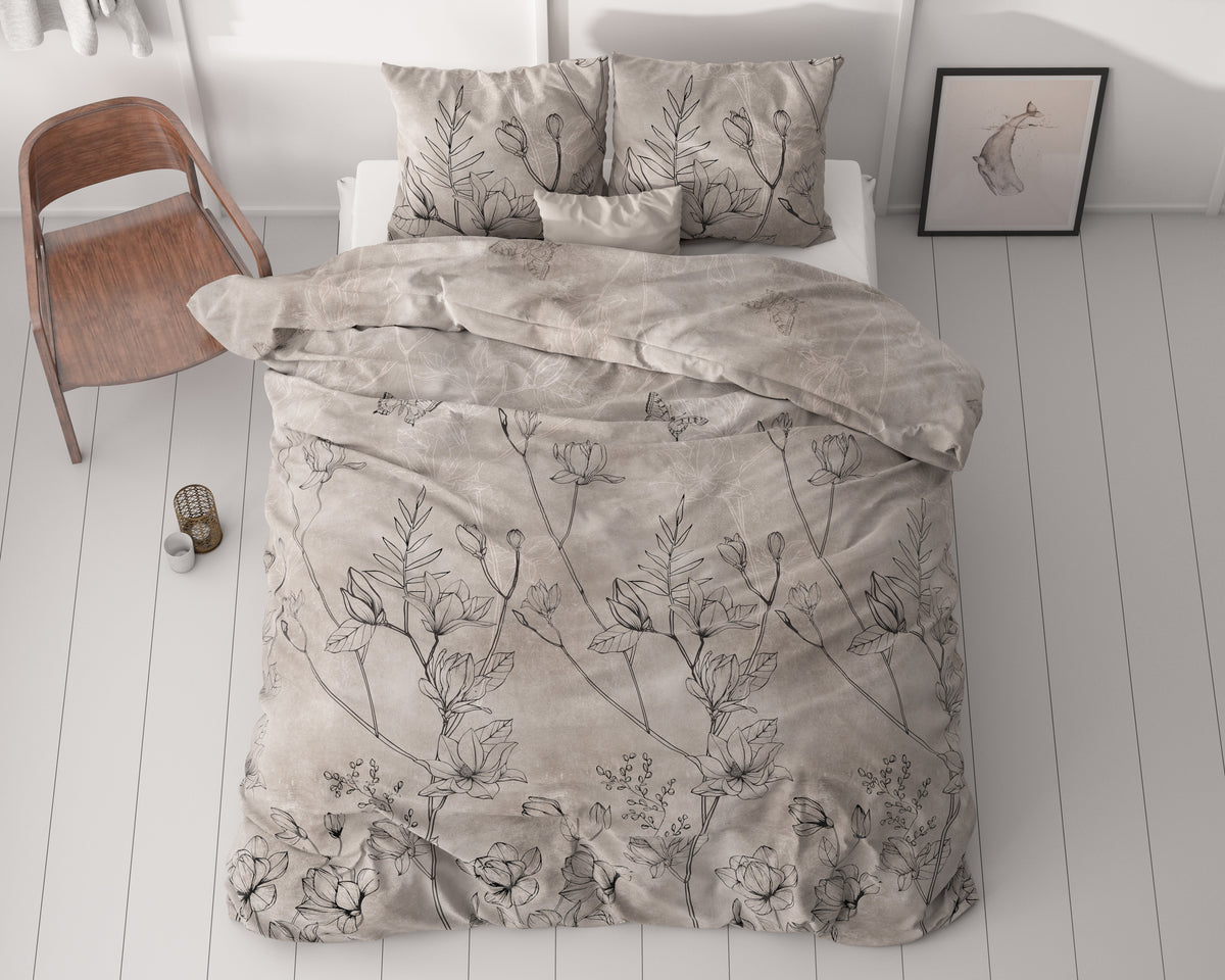Dekbedovertrek met zwarte bloemenprint op taupe ondergrond op een bed met kussens, naast een houten stoel