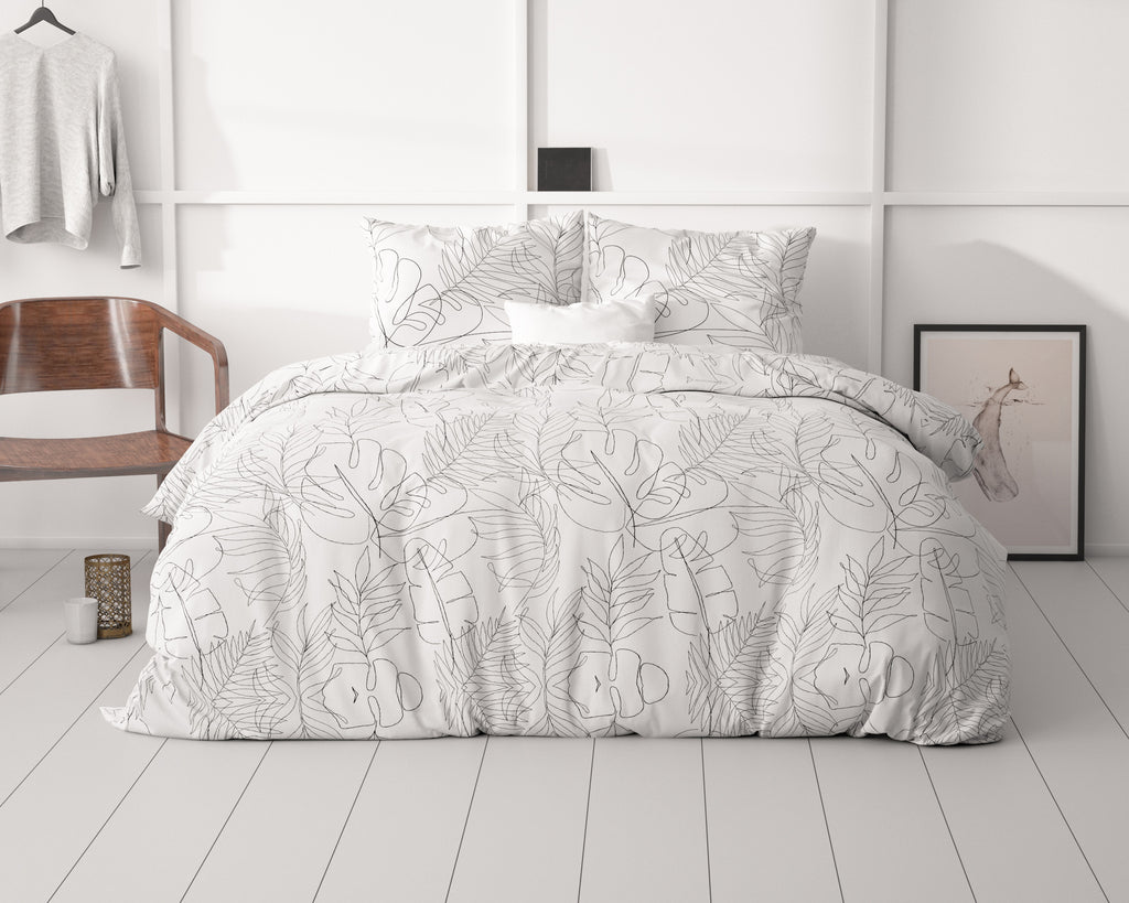 Opgemaakt bed met wit dekbedovertrek met zwarte lijntekening van bladeren en twee bijpassende kussens