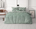 Bed met groen dekbedovertrek met zigzagpatroon en kussens, in een lichte slaapkamer met houten stoel