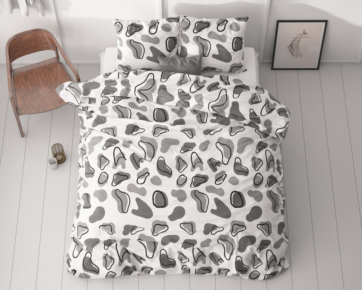 Dekbedovertrek met twee kussenslopen in wit met grijze en zwarte grafische vlekkenprint op een bed in een lichte slaapkamer