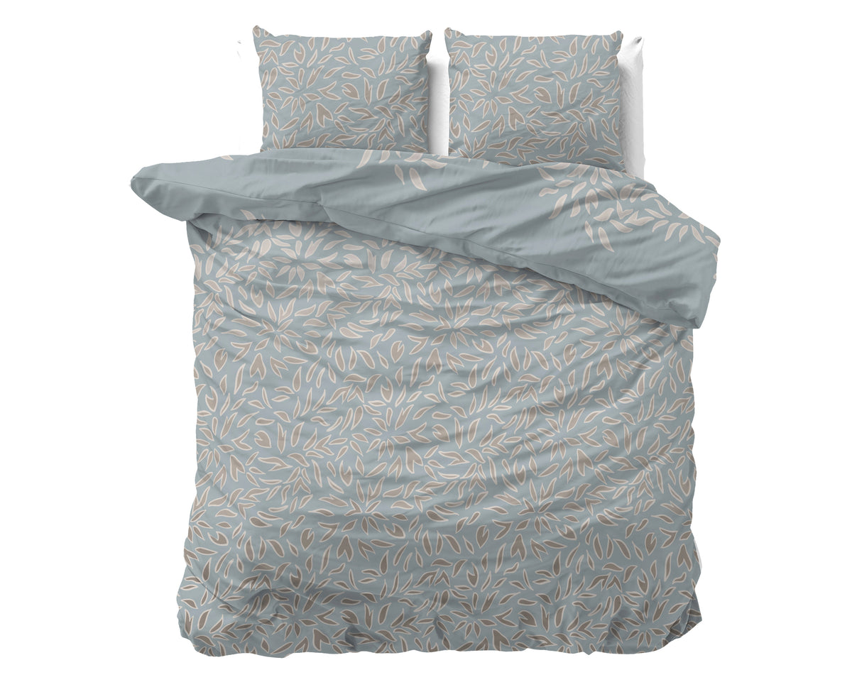 Blauw dekbedovertrek met beige en taupe bladprint, met twee bijpassende kussens op een bed