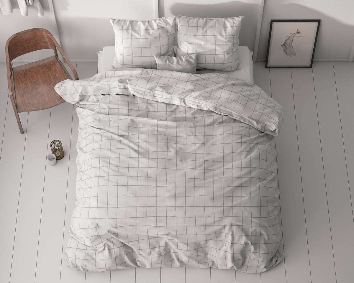 Bed met grijs geruit dekbedovertrek en kussens, gezien van boven, naast een houten stoel op een witte houten vloer