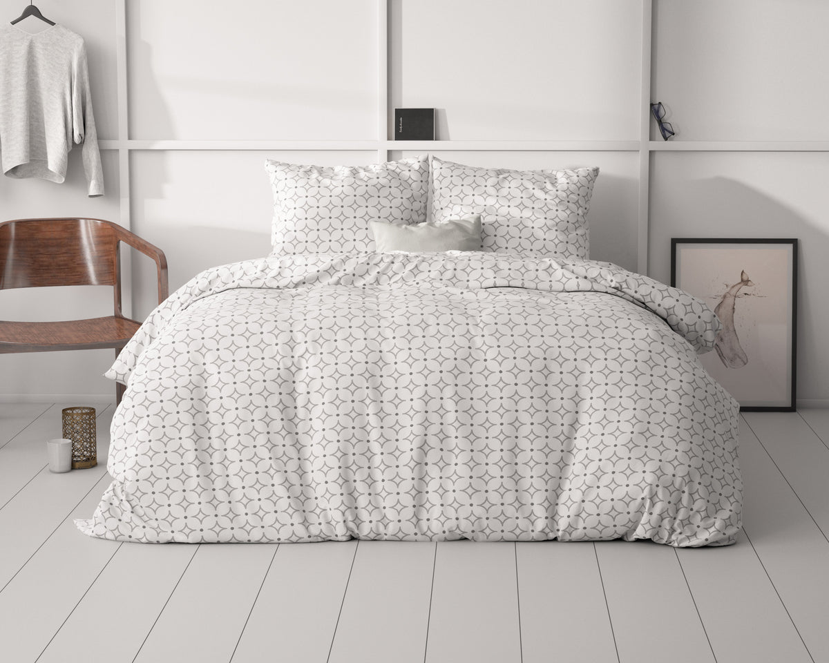 Bed met wit dekbedovertrek met grijs grafisch patroon en twee bijpassende kussenslopen in een lichte slaapkamer
