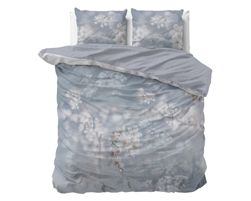 Dekbedovertrek Frost in grijsblauw met witte bloesemprint op een bed, met twee bijpassende kussens