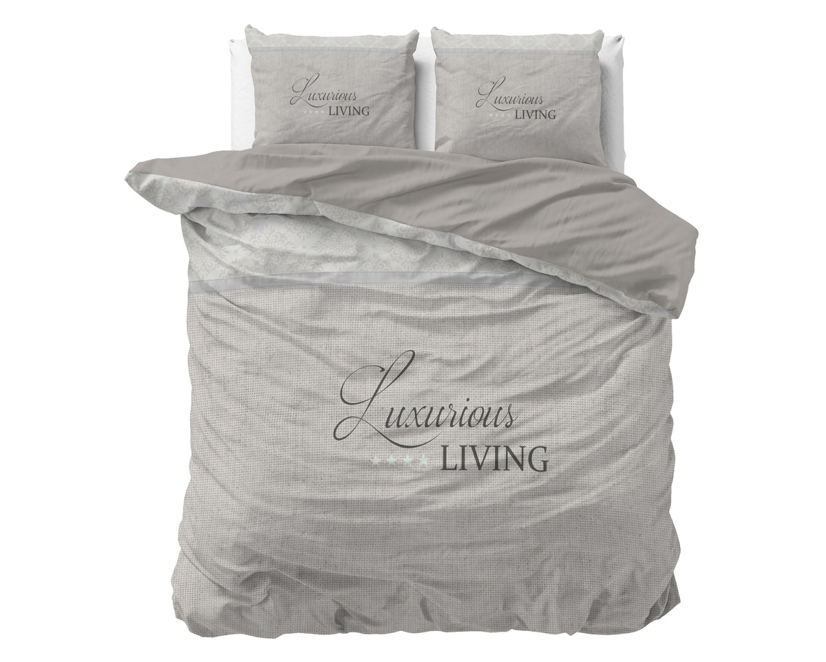 Dekbedovertrek in zand met de tekst Luxurious Living en twee bijpassende kussenslopen op een bed