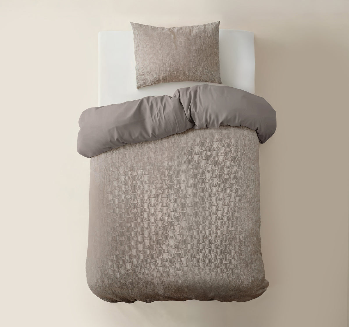 Taupe dekbedovertrek met grafisch motief en omgeslagen effen achterzijde, met bijpassende kussensloop op een wit matras