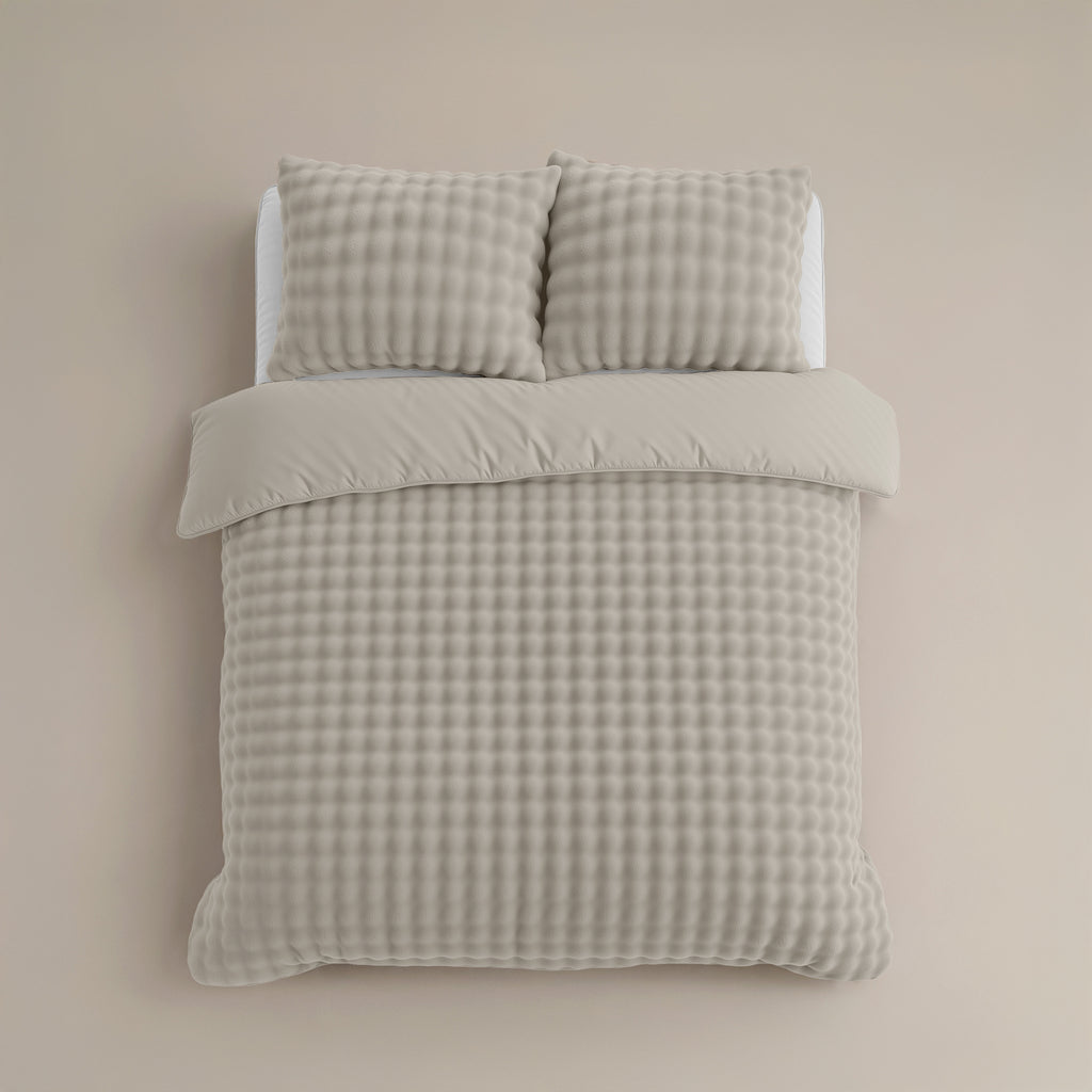 Beige dekbedovertrek met pompom-structuur en twee bijpassende kussenslopen op een bed, gezien van boven