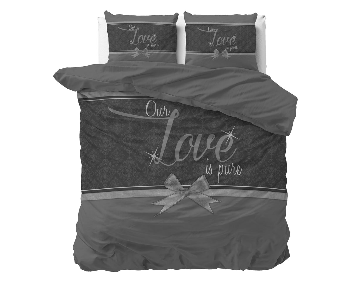 Grijs dekbedovertrek met de tekst Our Love is pure, een strik en patroon, met twee kussenslopen op een bed