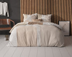 Bed met crème dekbedovertrek met strepen en beige vlakken, voor een houten lamellenwand in de slaapkamer
