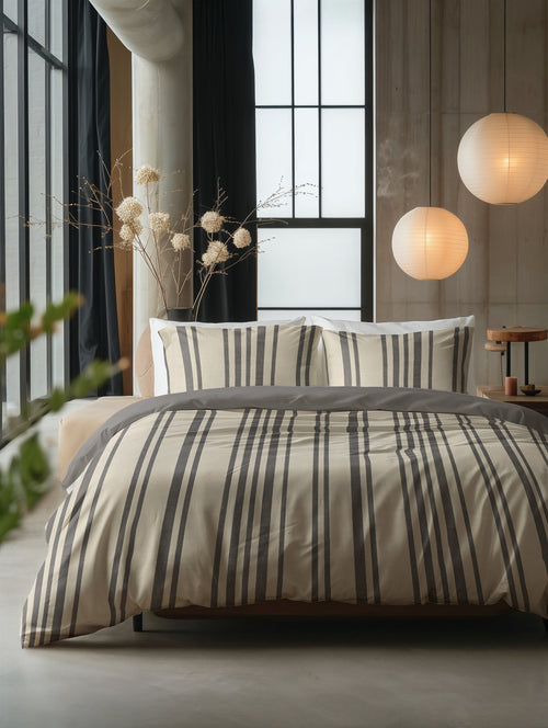 Bed met zandkleurig dekbedovertrek met grijze verticale strepen en twee bijpassende kussenslopen in een slaapkamer