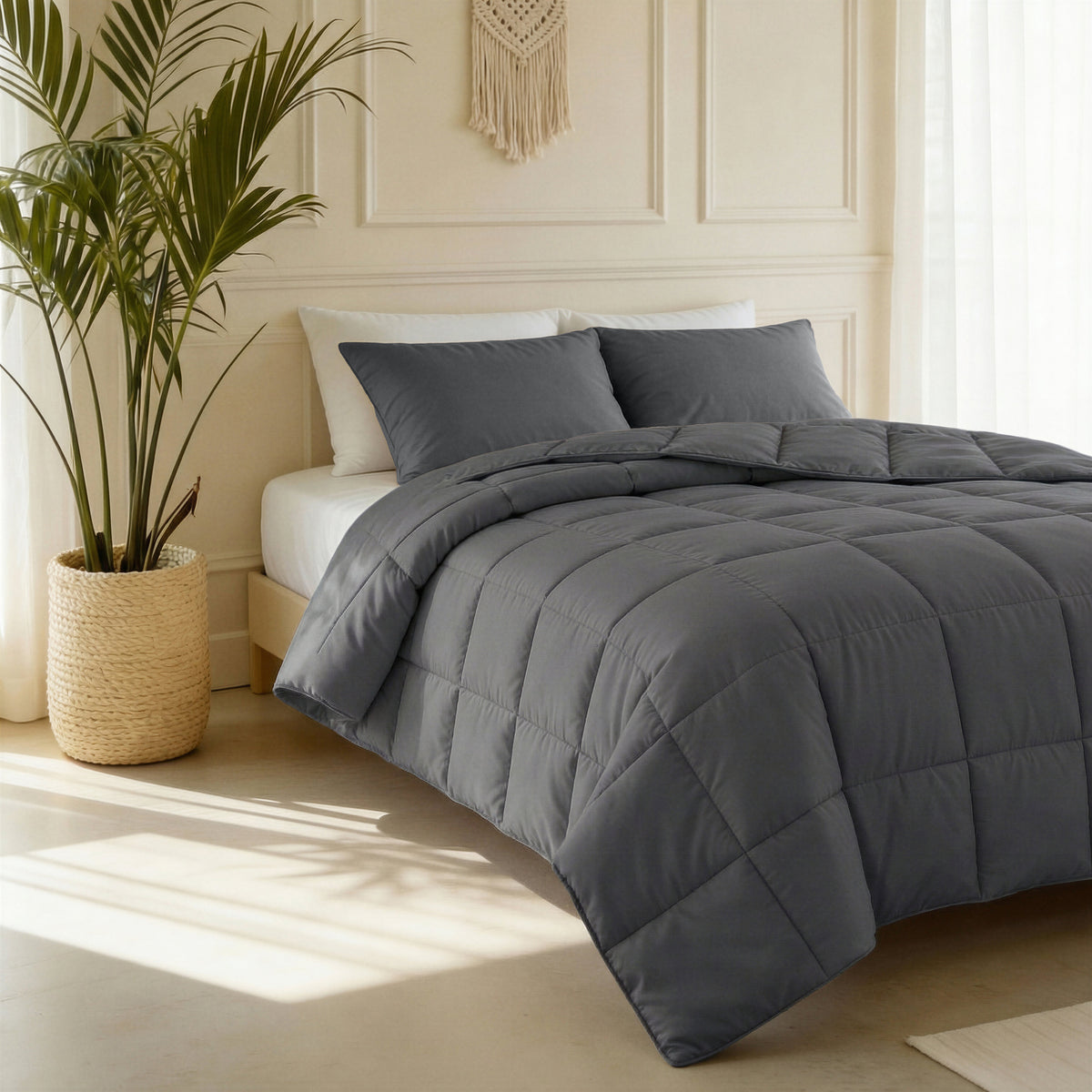 Antraciet gequilt dekbed met twee antraciete kussenslopen op een bed in een lichte slaapkamer met plant en rieten mand