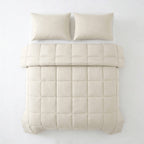 Beige gewatteerd lazy dekbed met blokjesstiksel op een bed, met twee beige kussens erboven, gezien van boven