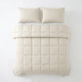 Beige lazy dekbed met vierkant stikpatroon en twee bijpassende kussens, van bovenaf gezien op een bed