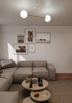 Plafondlamp met twee witte glazen bollen aan een gouden frame, brandend boven een woonkamer met bank en salontafels