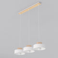 Witte hanglamp met drie ronde kappen met houten rand aan een langwerpige plafondplaat van hout en wit metaal