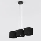 Zwarte hanglamp met drie stoffen cilinderkappen aan twee snoeren en een ronde plafondplaat