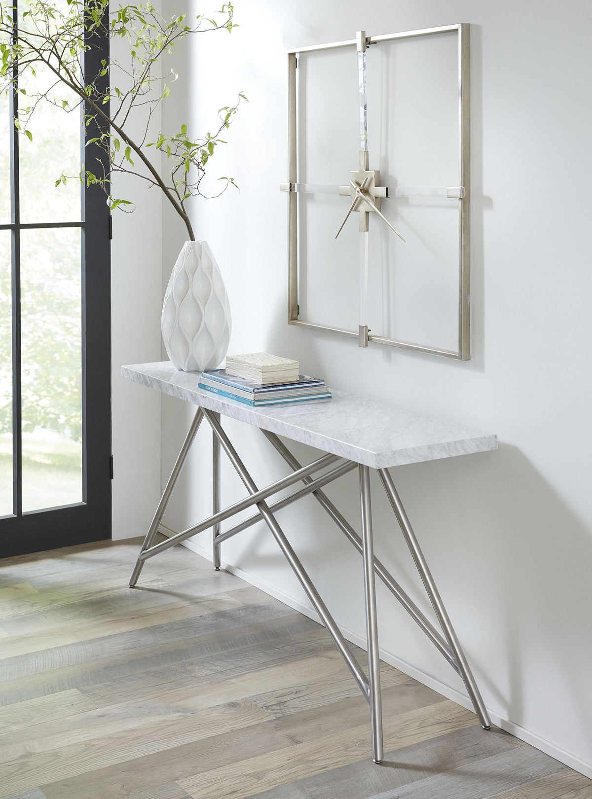 Witte marmeren consoletafel met roestvrijstalen frame in een hal, met vaas, boeken en een vierkante wandklok erboven