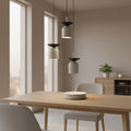 Drie grijze hanglampen met donkere bovenschaal op verschillende hoogtes boven een houten eettafel