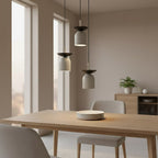 Drie grijze hanglampen met donkere bovenschaal op verschillende hoogtes boven een houten eettafel
