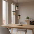 Drie beige hanglampen met donkere bovenkap boven een houten eettafel in een lichte eetkamer