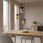 Drie beige hanglampen met donkere bovenkap boven een houten eettafel in een lichte eetkamer
