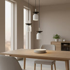 Drie witte hanglampen met zwarte schaal boven een houten eettafel in een lichte, rustig ingerichte ruimte