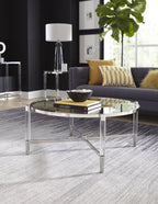 Ronde glazen salontafel met chromen rand en acrylpoten voor een grijze bank op een grijs vloerkleed