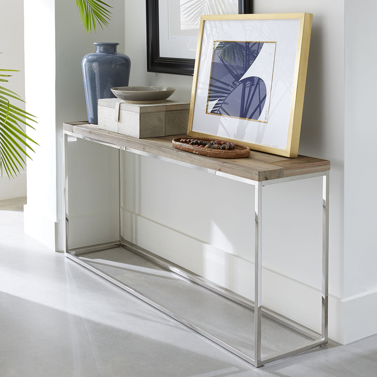 Consoletafel met houten blad en glanzend stalen frame, gestyled met blauwe vaas, kist, schaal en ingelijste print