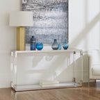 Transparante consoletafel met glazen blad en stalen rand in een woonkamer, met vazen, tafellamp en schilderij erboven