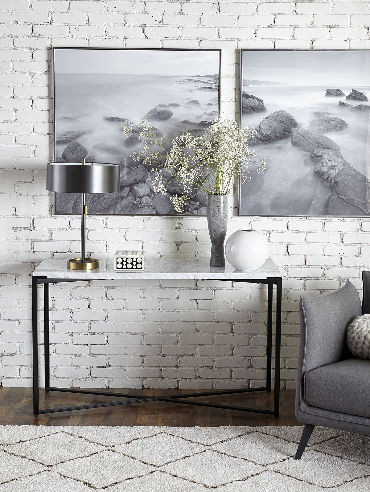 Consoletafel met wit marmeren blad en zwart metalen X-frame, met lamp en vazen, tegen een witte bakstenen muur