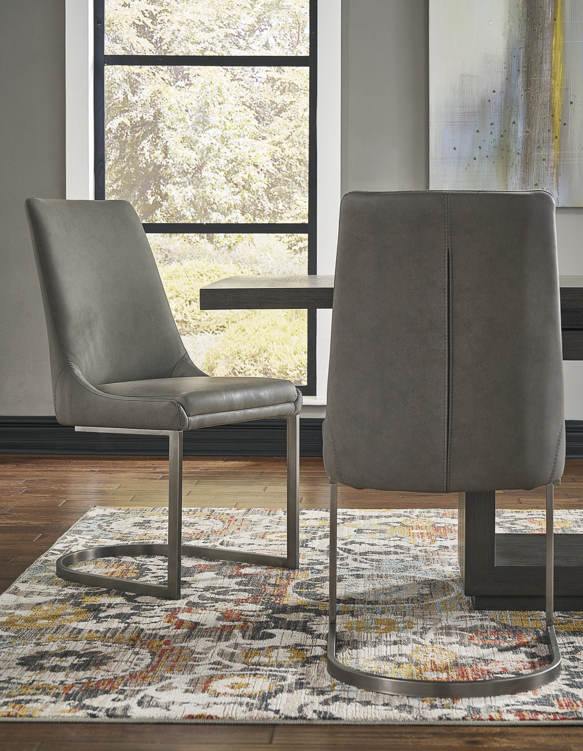 Twee grijze eetkamerstoelen met metalen vrijdragend onderstel naast een donkere eettafel, een van voren en een van achteren