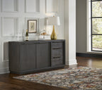 Basaltgrijs dressoir met deuren en lades, met lamp, wijnglazen en cakestolp erop, naast een vloerkleed