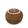 Ronde opbergmand van bruin gevlochten rotan met deksel en een rand van witte cowrieschelpen