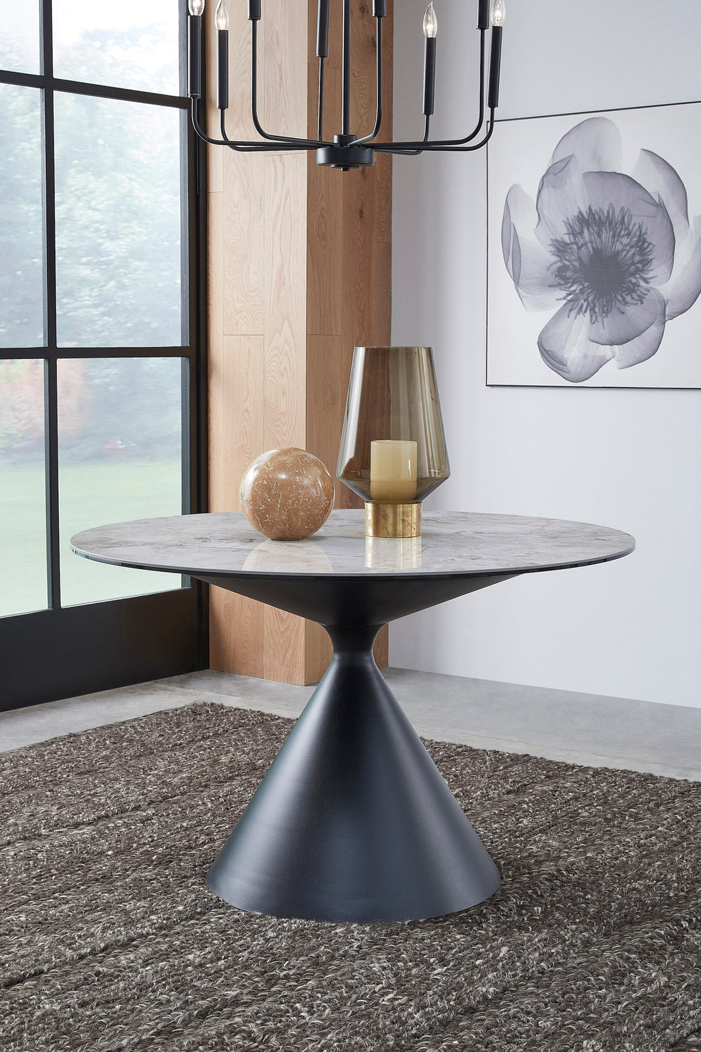 Ronde eettafel met grijs marmerpatroon blad en zwart uurglasvormig onderstel, met glazen lantaarn en decoratieve bol erop