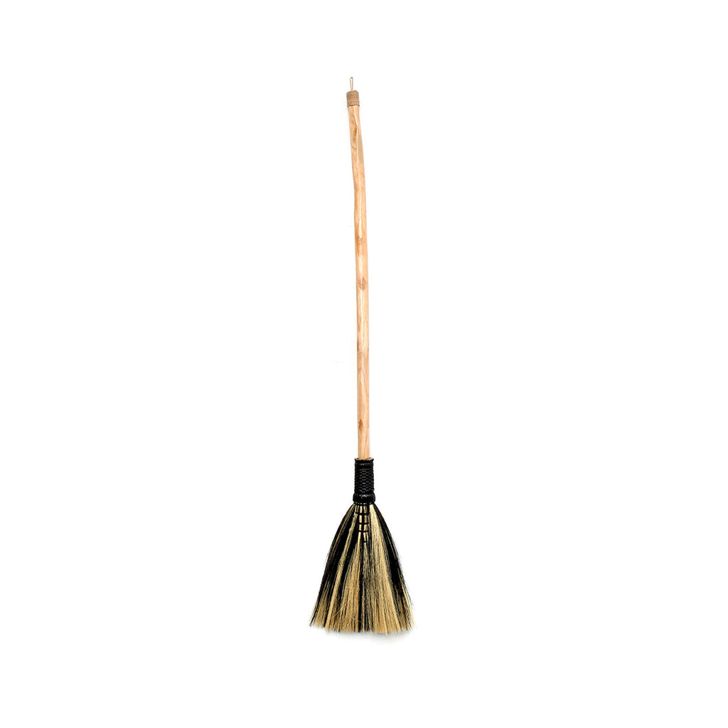 Bezem met lange houten steel en tweekleurige zwart-naturel grasvezels op een witte achtergrond