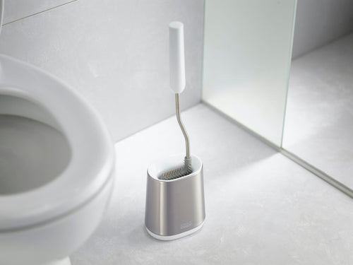 Toiletborstel met wit handvat en flexibele kop in een zilverkleurige houder naast een wit toilet