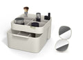 Grijze make-up organiser met vakken en lade, gevuld met kwast en make-up, naast een opengeklapte handspiegel