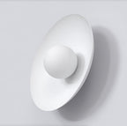Witte wandlamp met ovale rugplaat en ronde witte bol aan een lichtgrijze wand