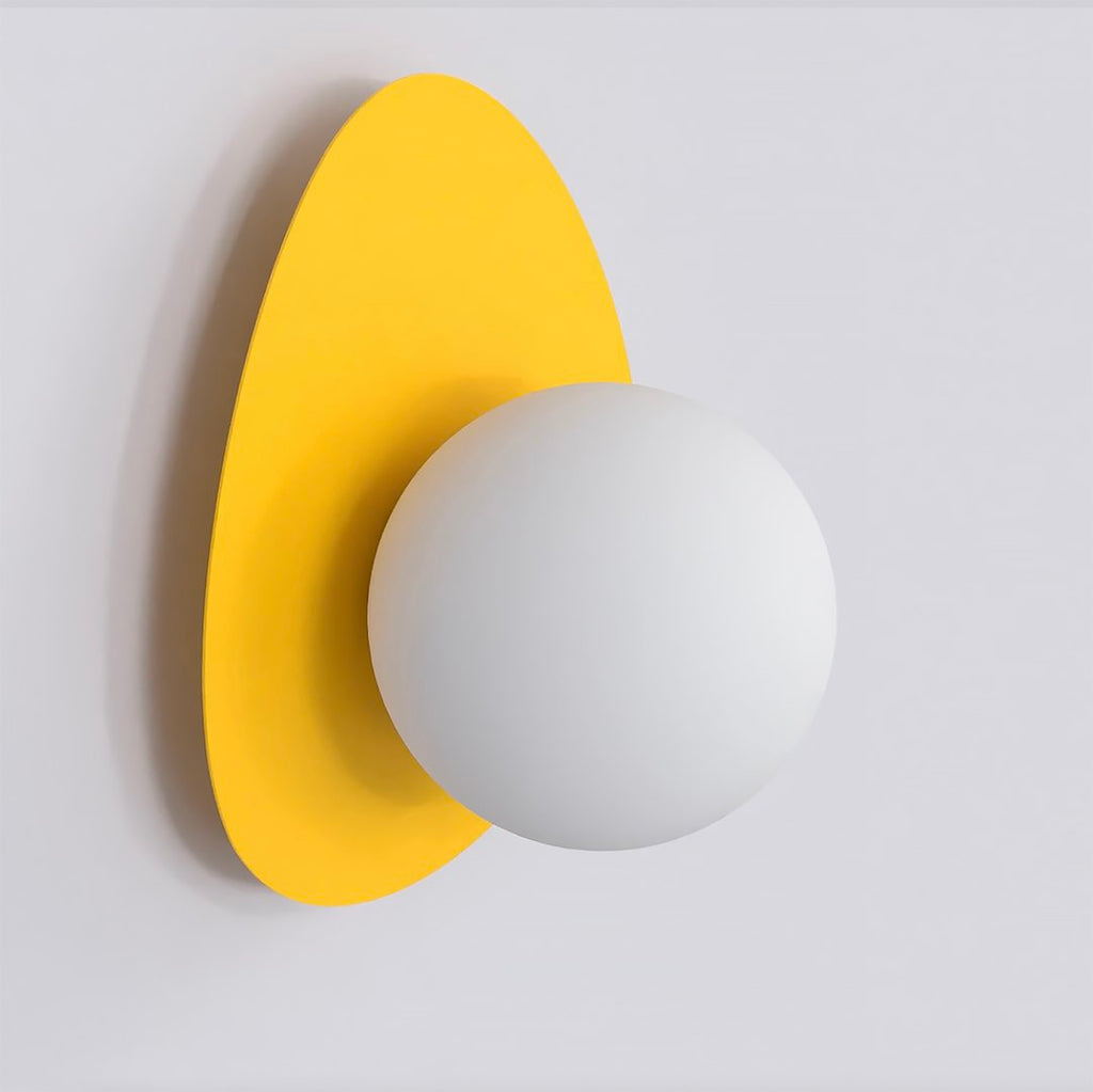 Wandlamp met witte ronde bol op een keivormige gele achterplaat tegen een lichte muur