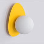 Wandlamp met witte ronde bol op een keivormige gele achterplaat tegen een lichte muur