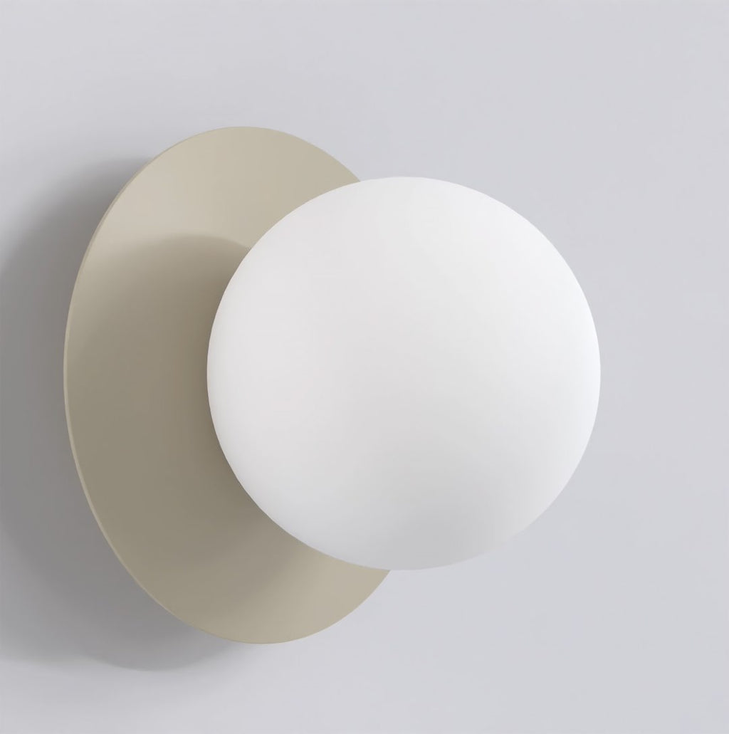 Wandlamp met witte bol voor een ronde achterplaat in mokka tegen een lichtgrijze muur