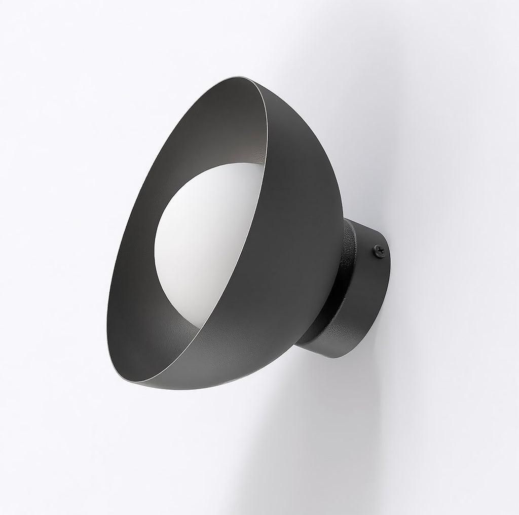 Zwarte wandlamp met schuin geplaatste komvorm en witte bolvormige lampenkap, gemonteerd op een lichte muur