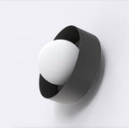 Zwarte wandlamp met witte bolkap in een gedraaide metalen band tegen een lichte muur