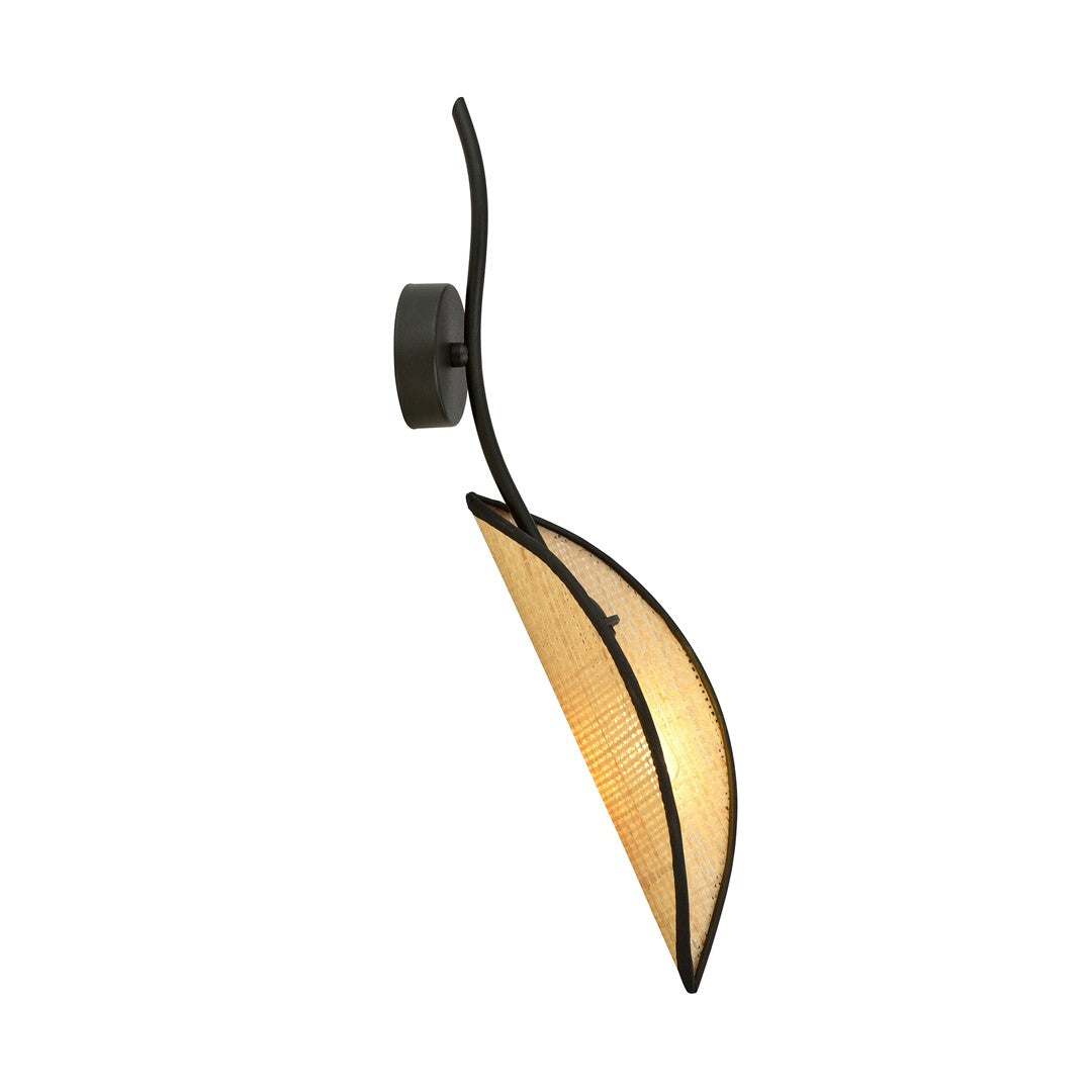 Zwarte wandlamp met gebogen stalen arm en bladvormige rotan kap die warm licht geeft