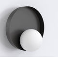 Zwarte ronde wandlamp met witte bol die voor de metalen schijf zit