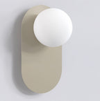 Wandlamp met matte witte bol op een langwerpige, afgeronde montageplaat in mokka tegen een lichtgrijze wand