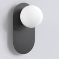 Zwarte wandlamp met langwerpige achterplaat en matte witte bol, aan een lichtgrijze muur