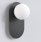 Zwarte wandlamp met langwerpige achterplaat en matte witte bol, aan een lichtgrijze muur