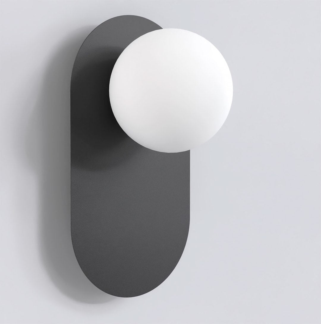 Zwarte wandlamp met langwerpige achterplaat en matte witte bol, aan een lichtgrijze muur