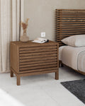 Houten nachtkastje met lamellenfront naast een bed met bijpassend lamellen hoofdbord